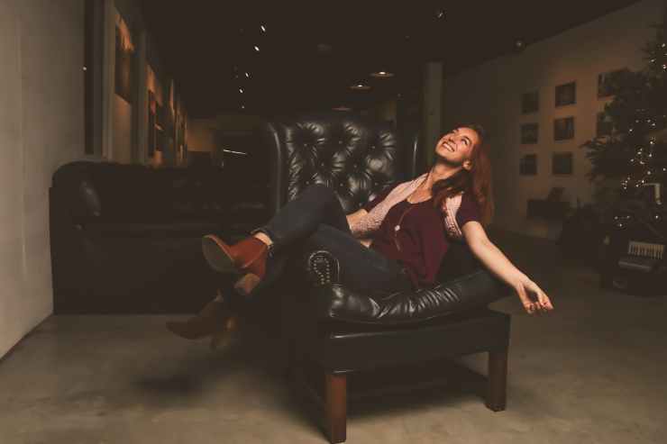 woman in maroon scoop neck shirt sitting on black leather sofa chair